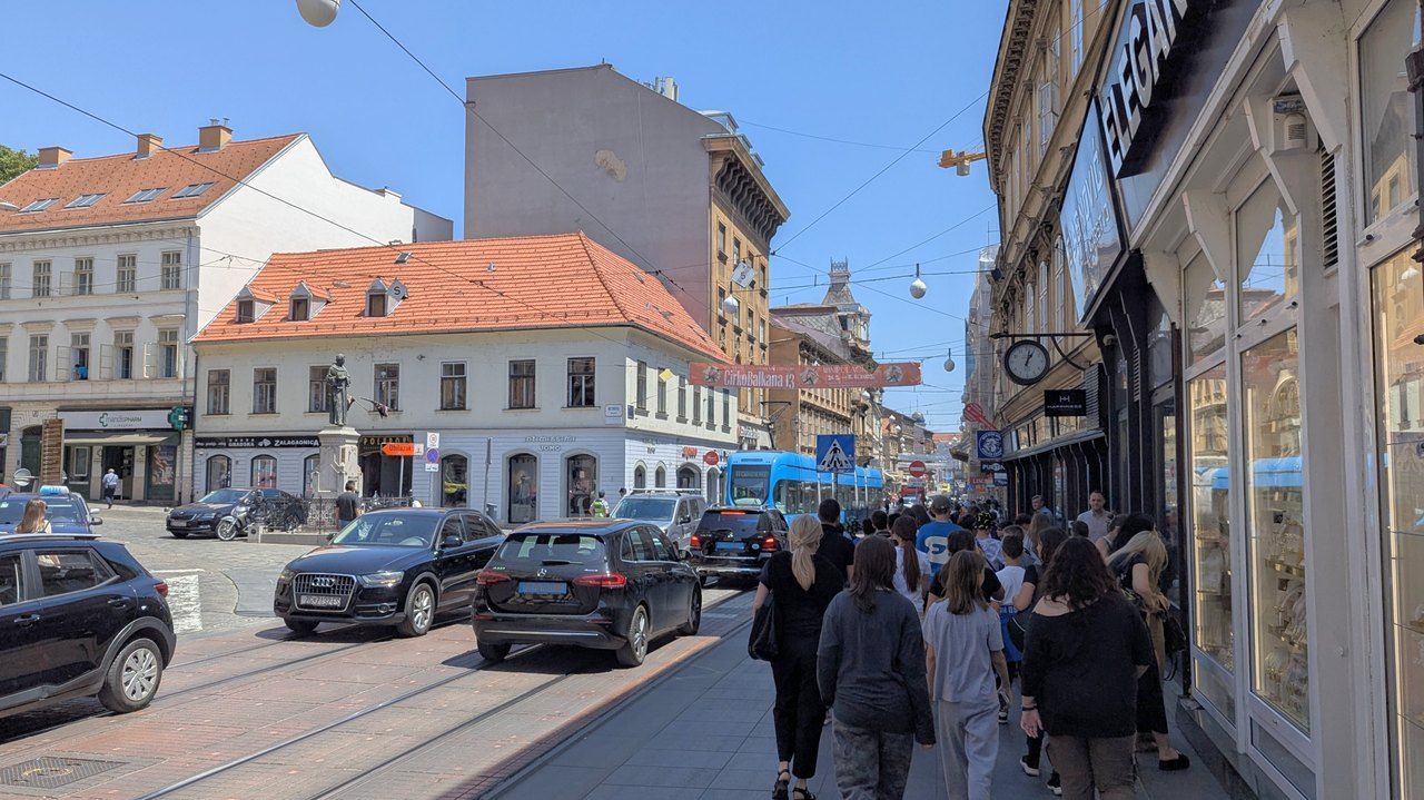 Ulica u središtu Zagreba za sunčana dana: tramvaj, parkirani automobili i pješaci na pločniku snimljeni s leđa