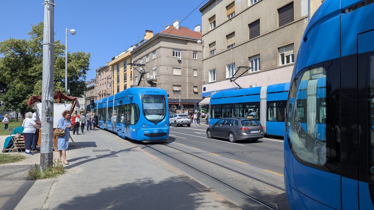 Zagrebačka ulica po sunčanom danu, plavi tramvaji, parkirani automobili, stambene zgrade i drveće